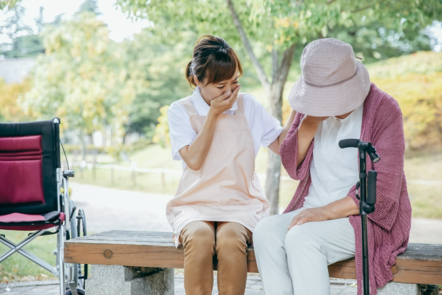 ベンチに座って悲しむ高齢者と介護士