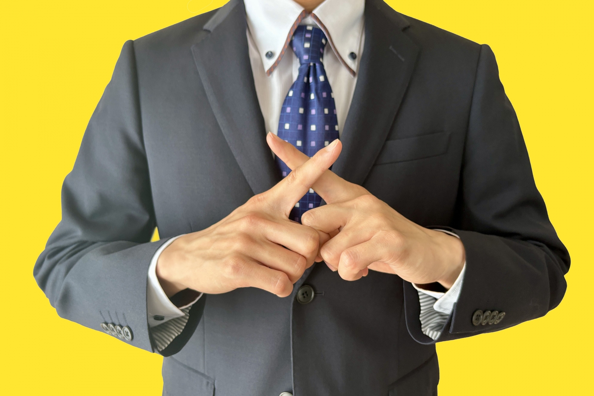 指でバツサインをするスーツの男性