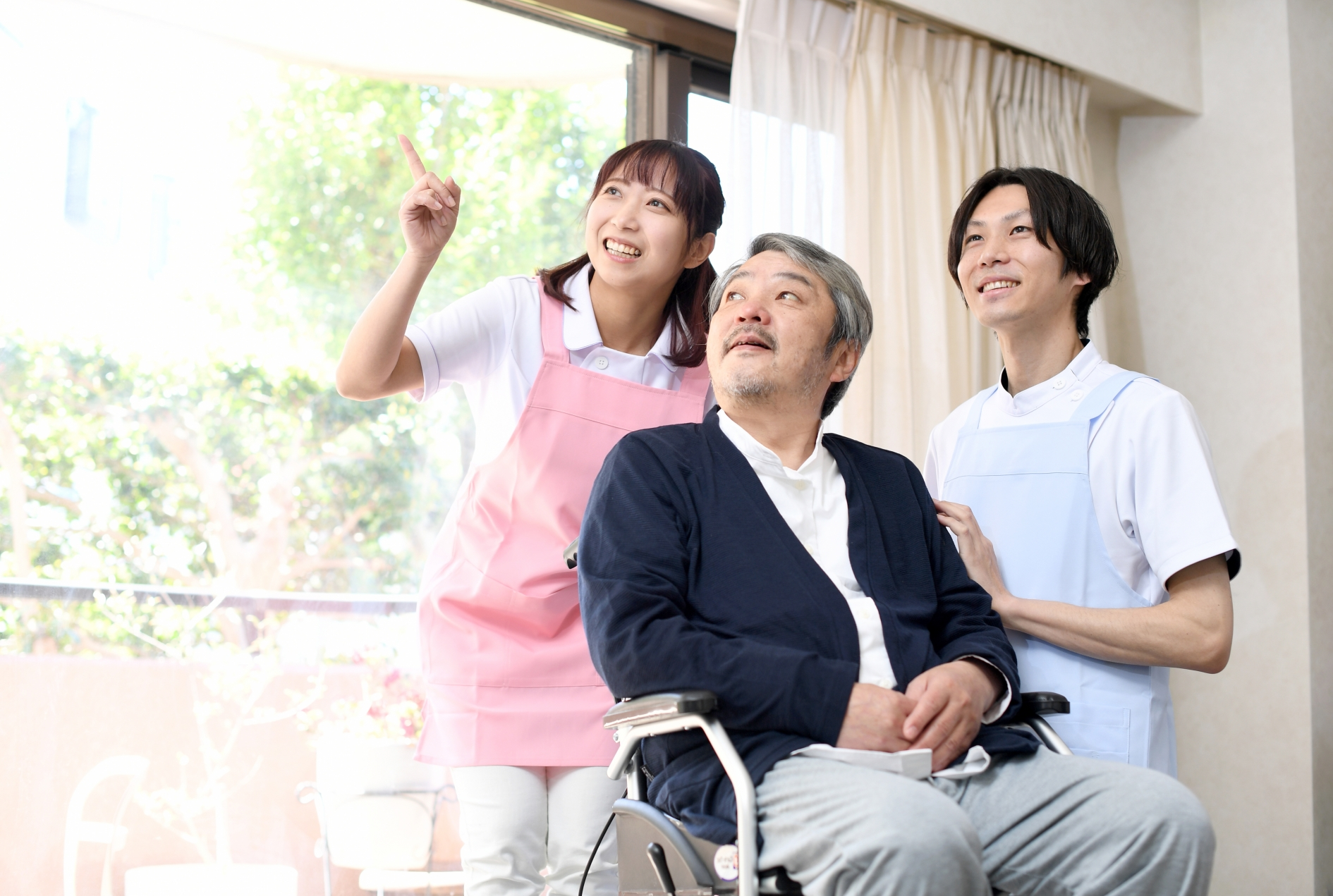 車椅子に乗る高齢者の男性と男女の介護士
