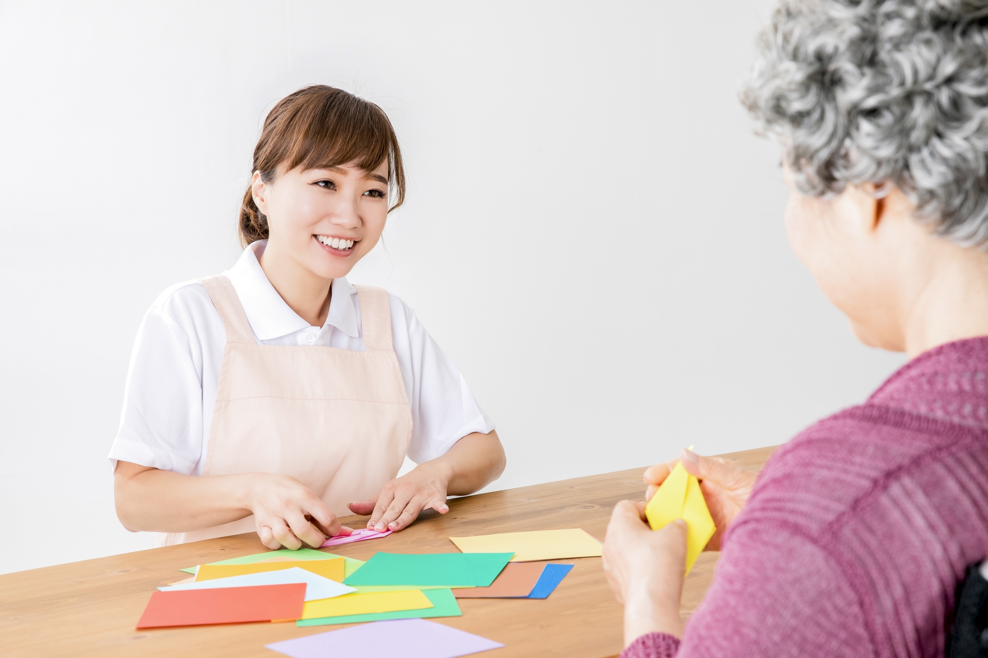 折り紙でレクリエーションする介護士と高齢者の女性