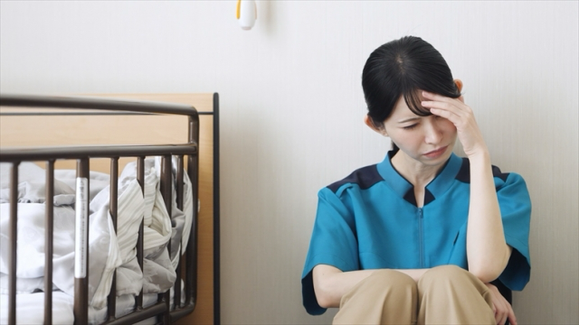 部屋の隅で座って頭を抱える女性