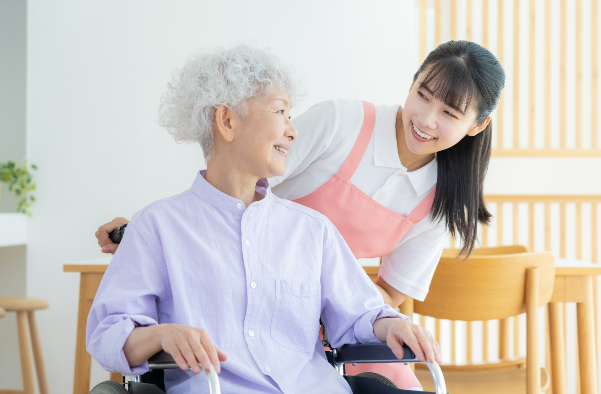 車椅子の女性の後ろから笑顔で話しかけるスタッフ
