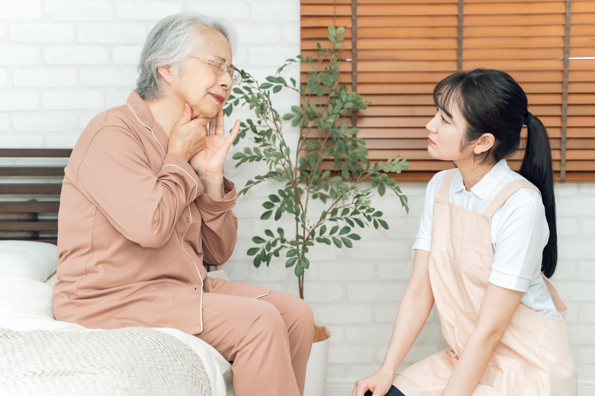 痛がる高齢者女性とエプロン姿の女性