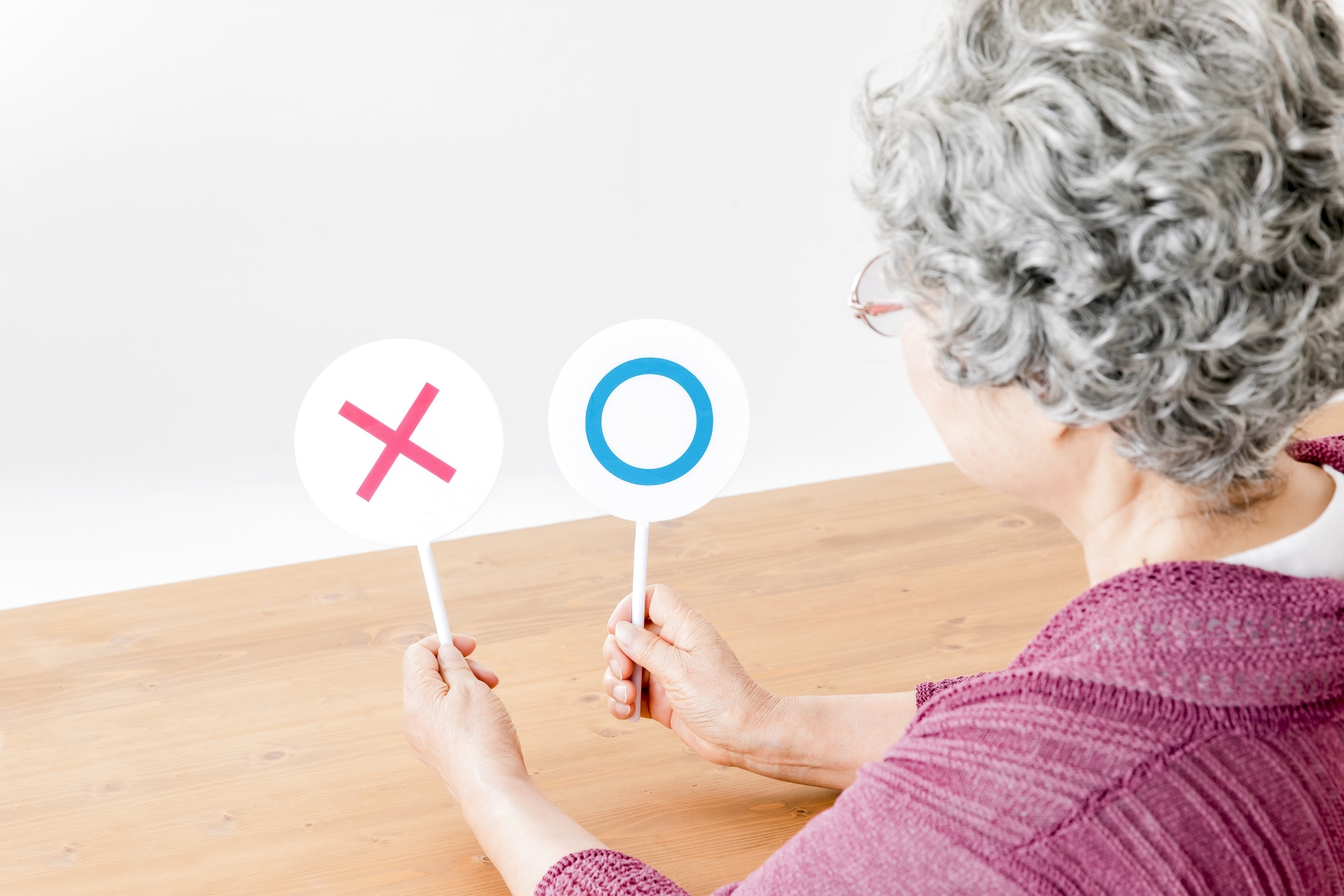 まるとバツの札を持つシニアの女性