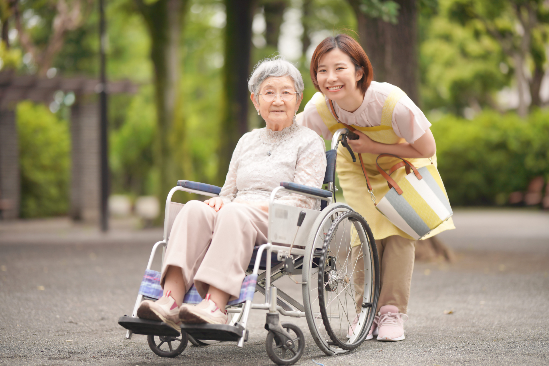 屋外にいる笑顔の介護士と車椅子の女性