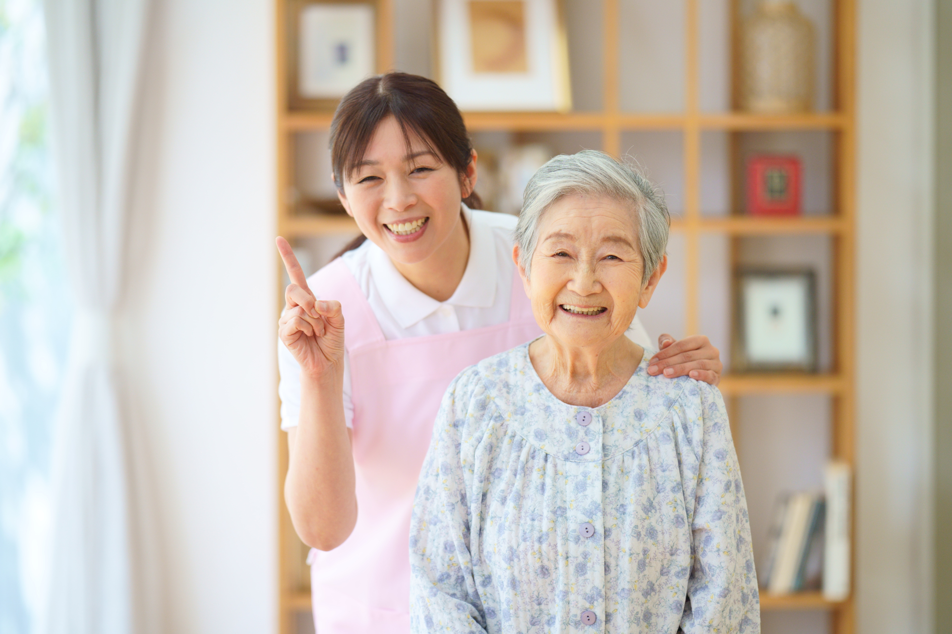 一番のポーズをする介護士と高齢女性
