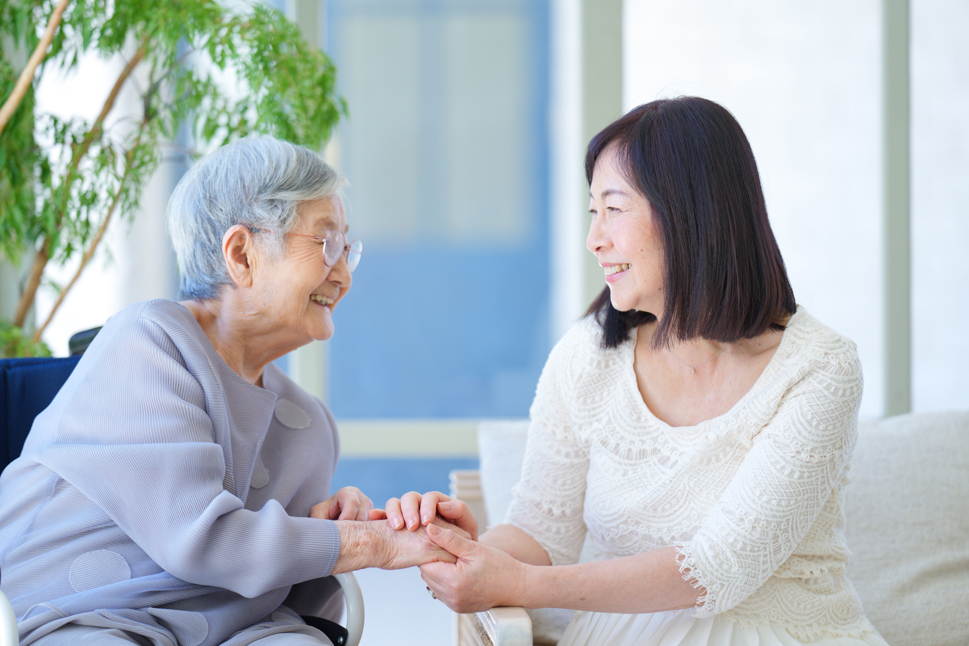 車椅子に乗っている高齢女性と手を握る中年女性