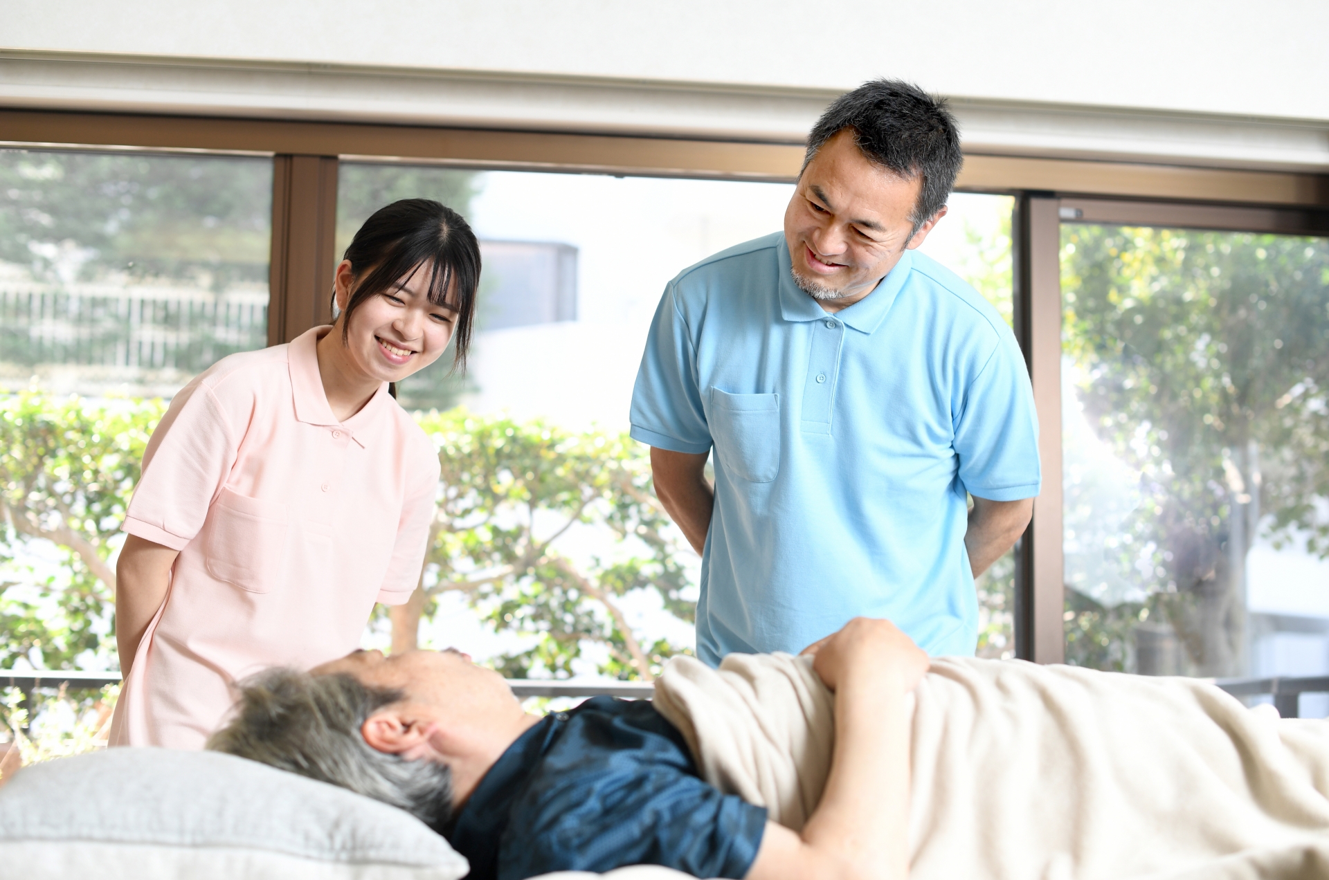 横になる高齢男性を見守る介護士たち