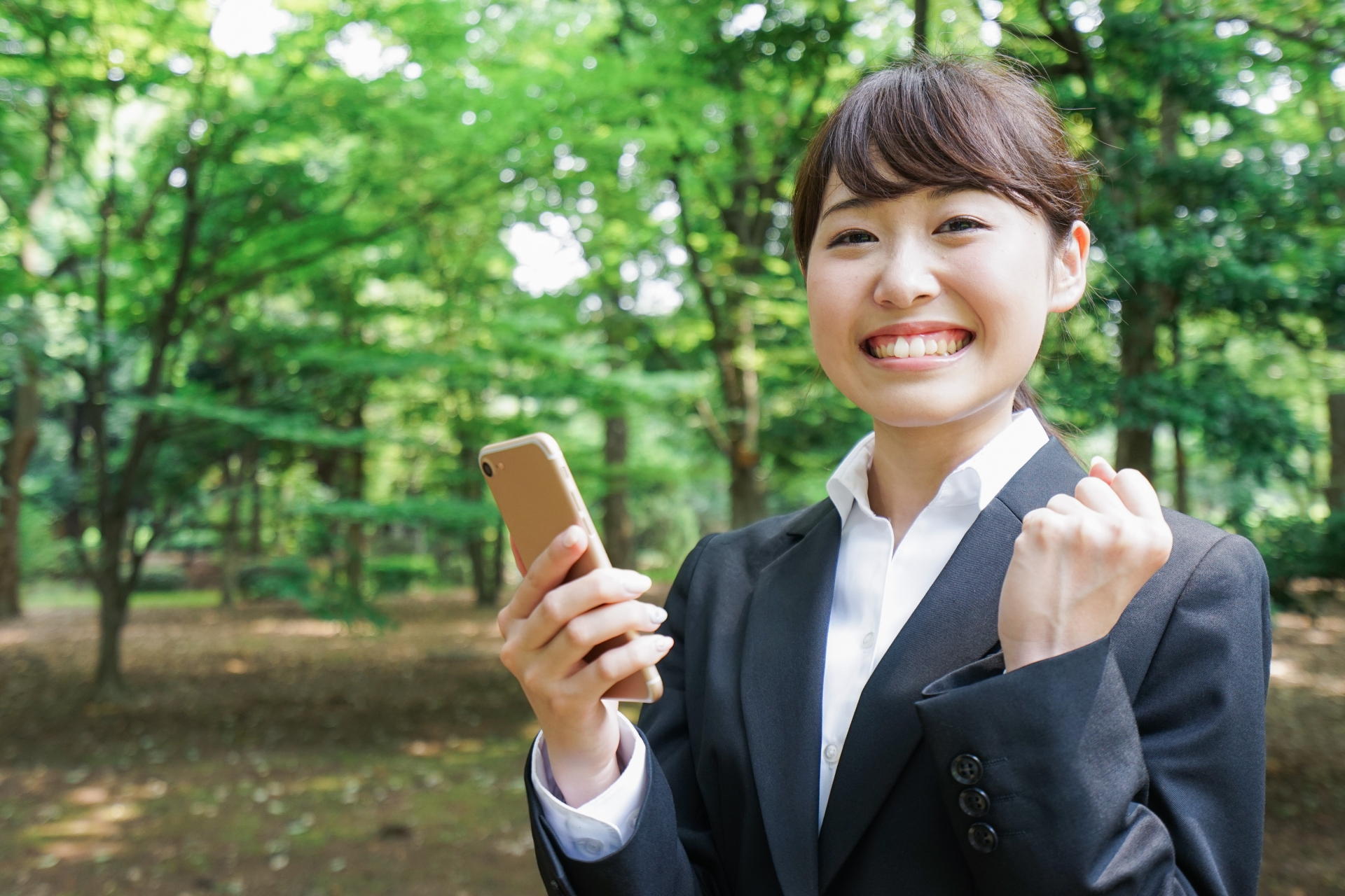 スマホを手にガッツポーズをするスーツの女性