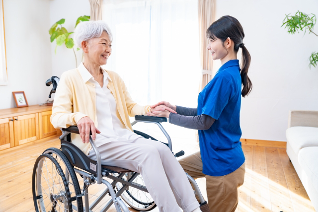 車椅子の女性の手を取る介護士