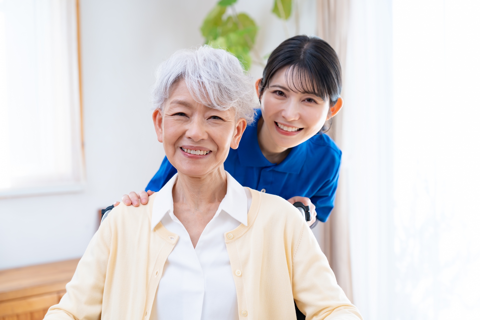 高齢者の後ろから顔を覗かせる笑顔の女性スタッフ
