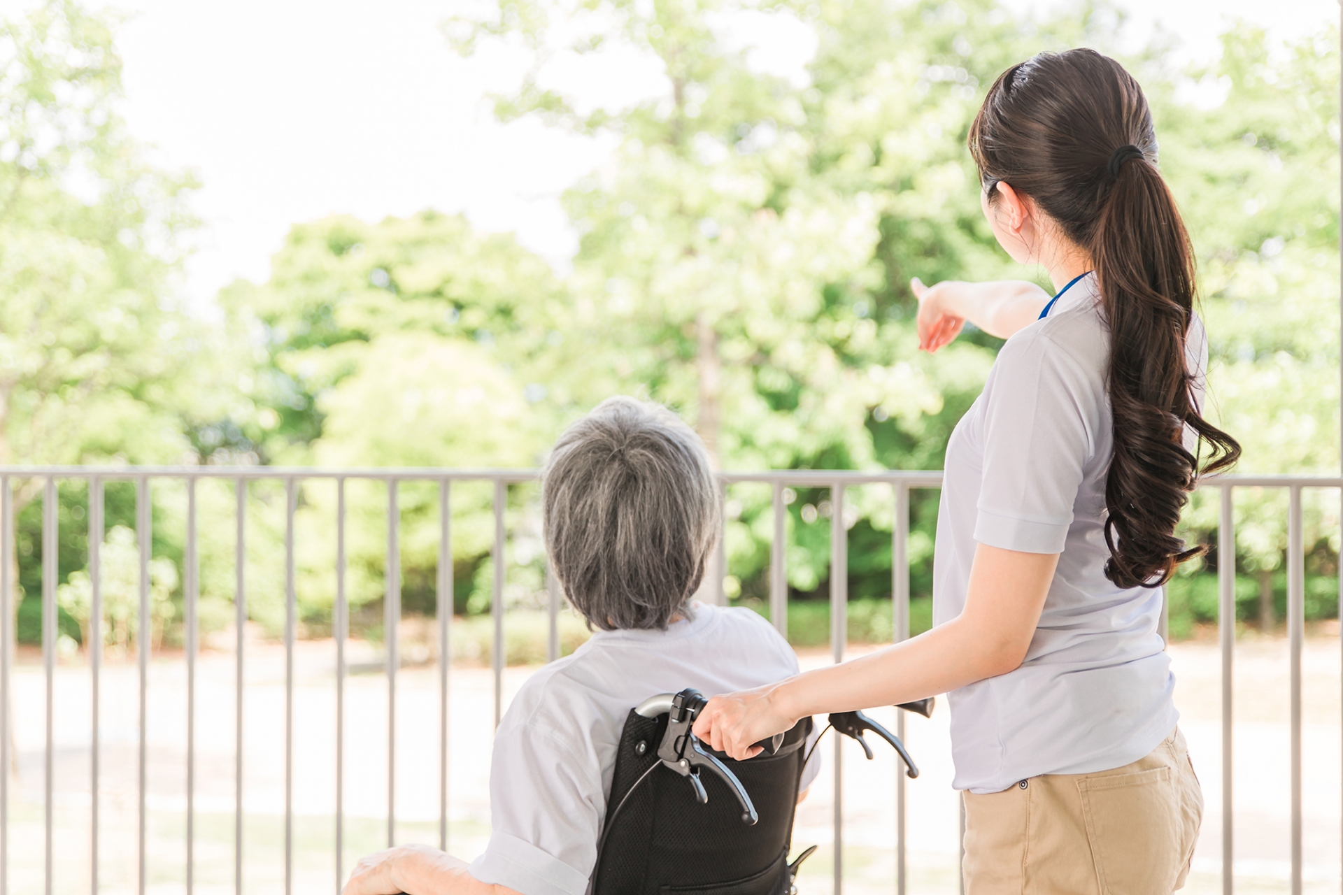 ベランダに出て外を見る車椅子の人と介護士