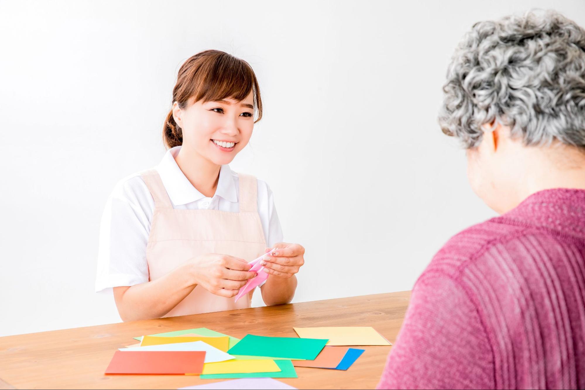 折り紙でレクリエーションする介護士と高齢者の女性
