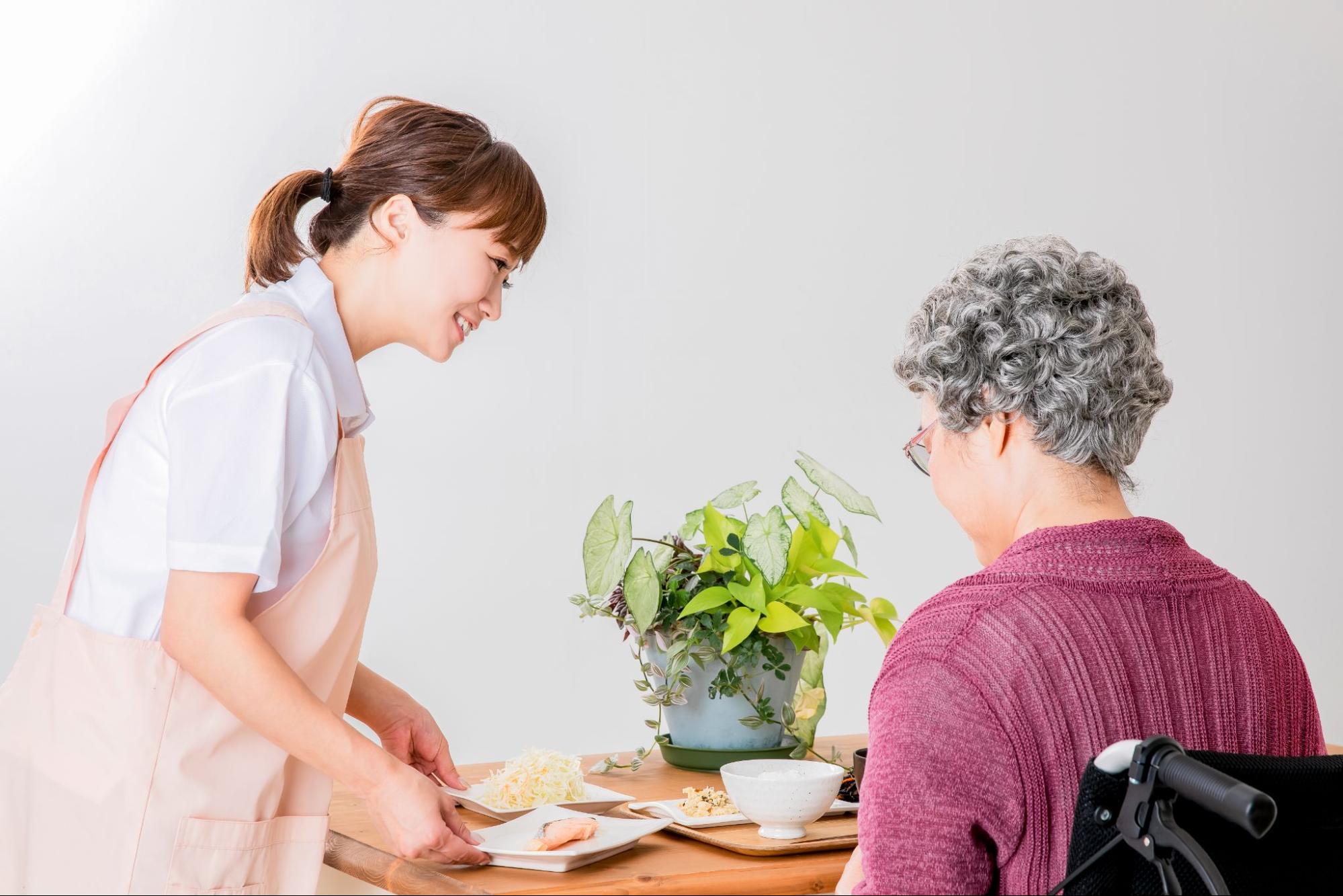 高齢者の女性と食事を運ぶ介護士・ヘルパー