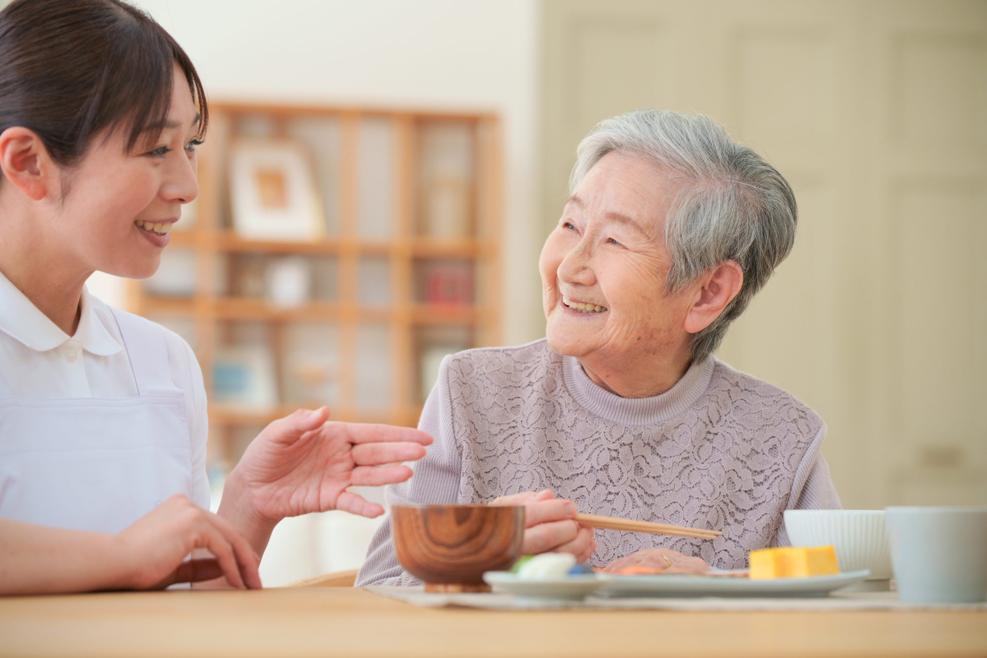 食事中の女性に話し掛ける介護士
