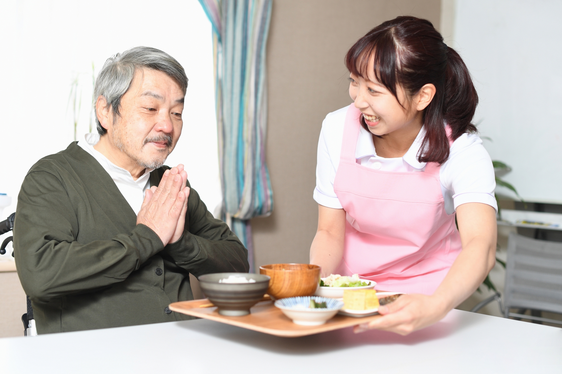 食事の配膳をする女性介護士と高齢者男性