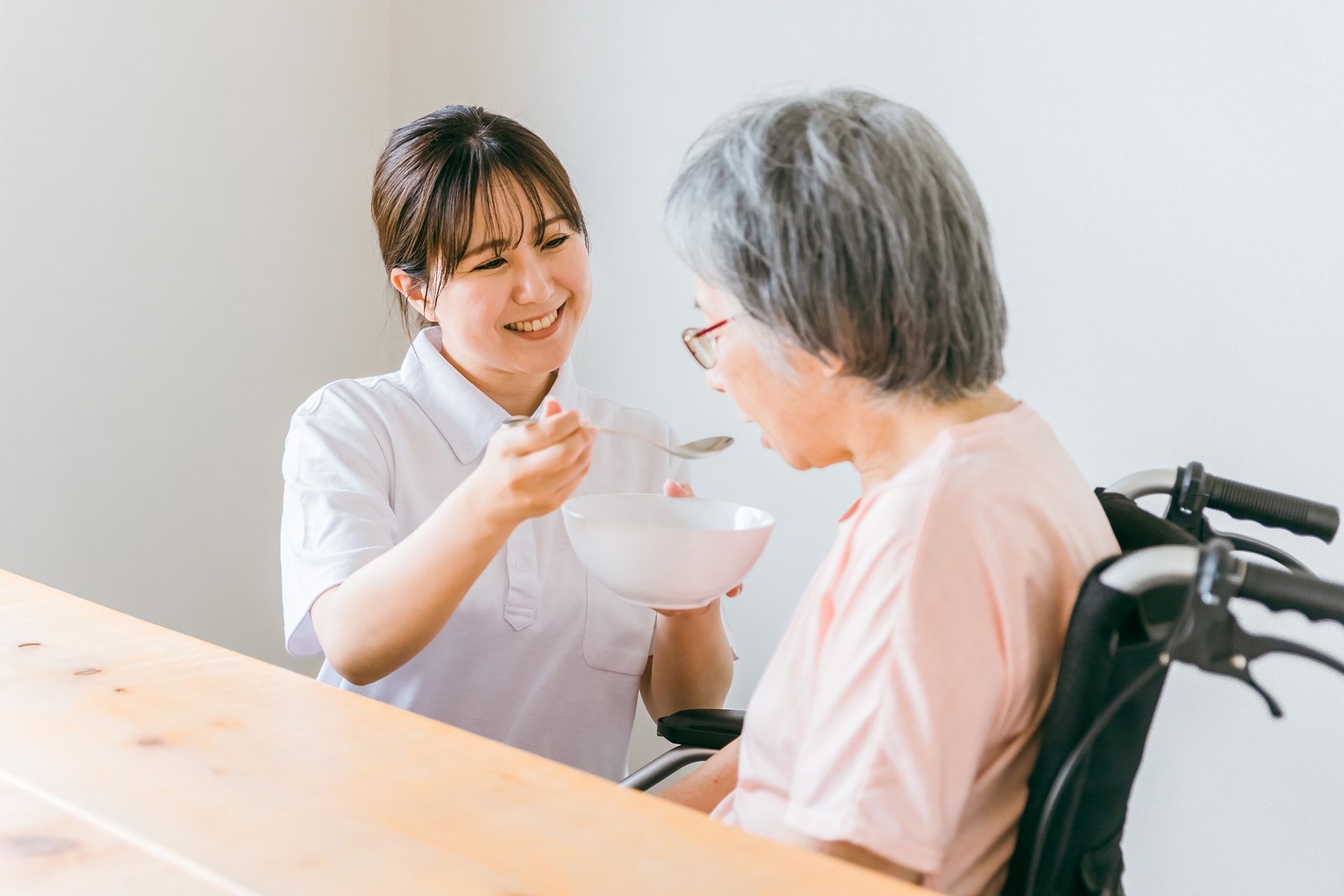 食事する高齢者女性と食事介助するヘルパー