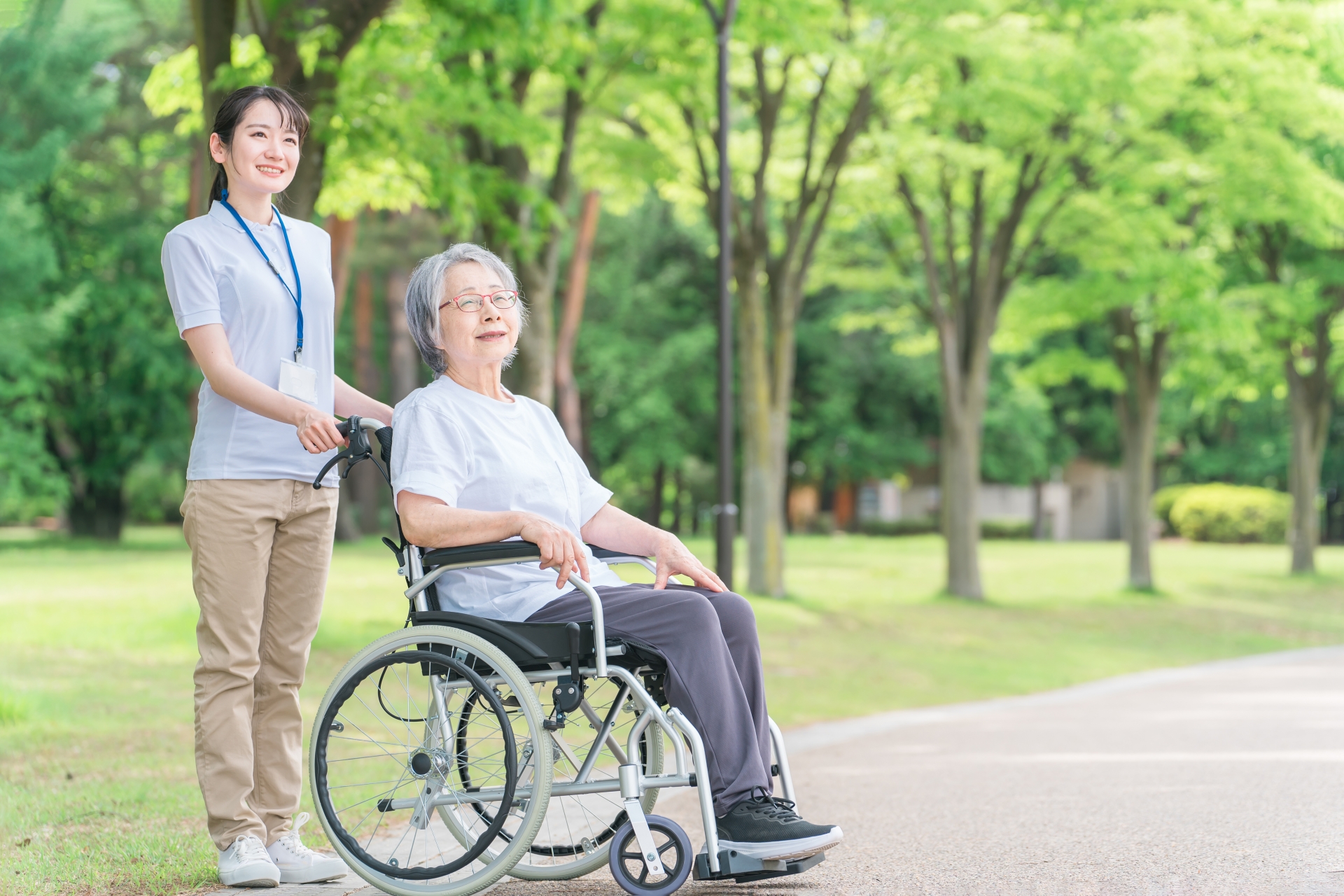 公園を散歩する車椅子の高齢者と介護士
