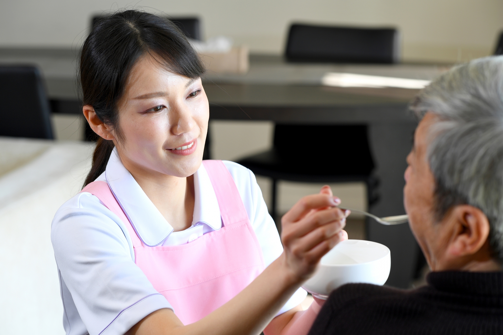 シニア男性に食事の介助をするエプロン姿の若い女性