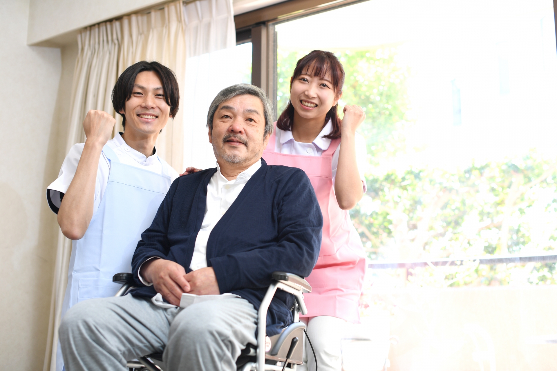 老人ホームで車椅子に乗る高齢者の男性と男女の介護士