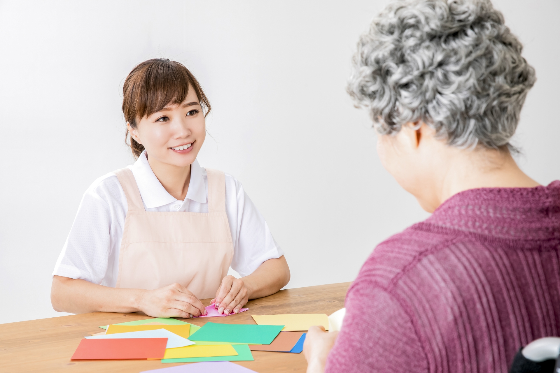 折り紙でレクリエーションする介護士と高齢者の女性