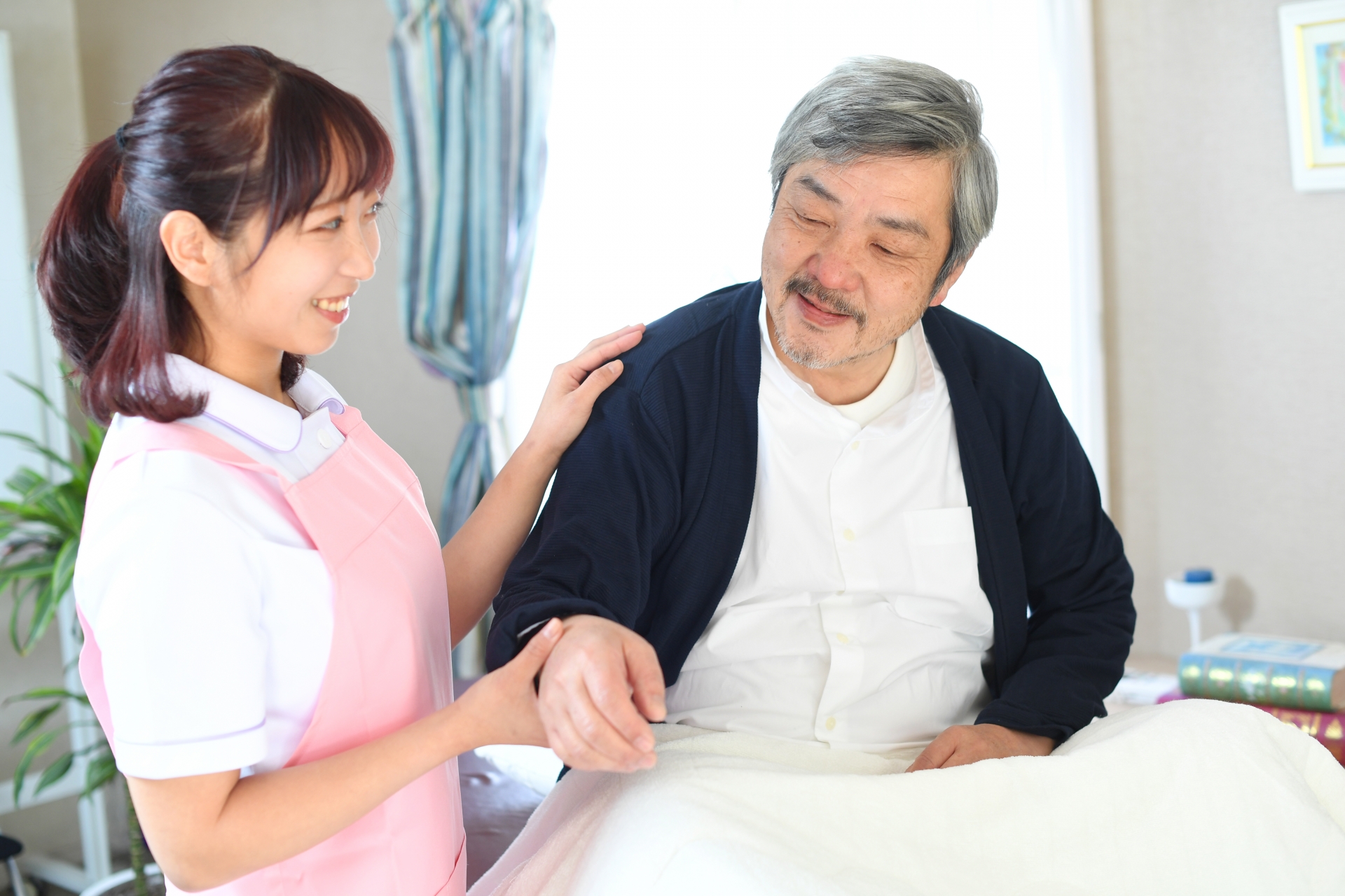 ベッドで寝たきりのお年寄りと介護士の女性