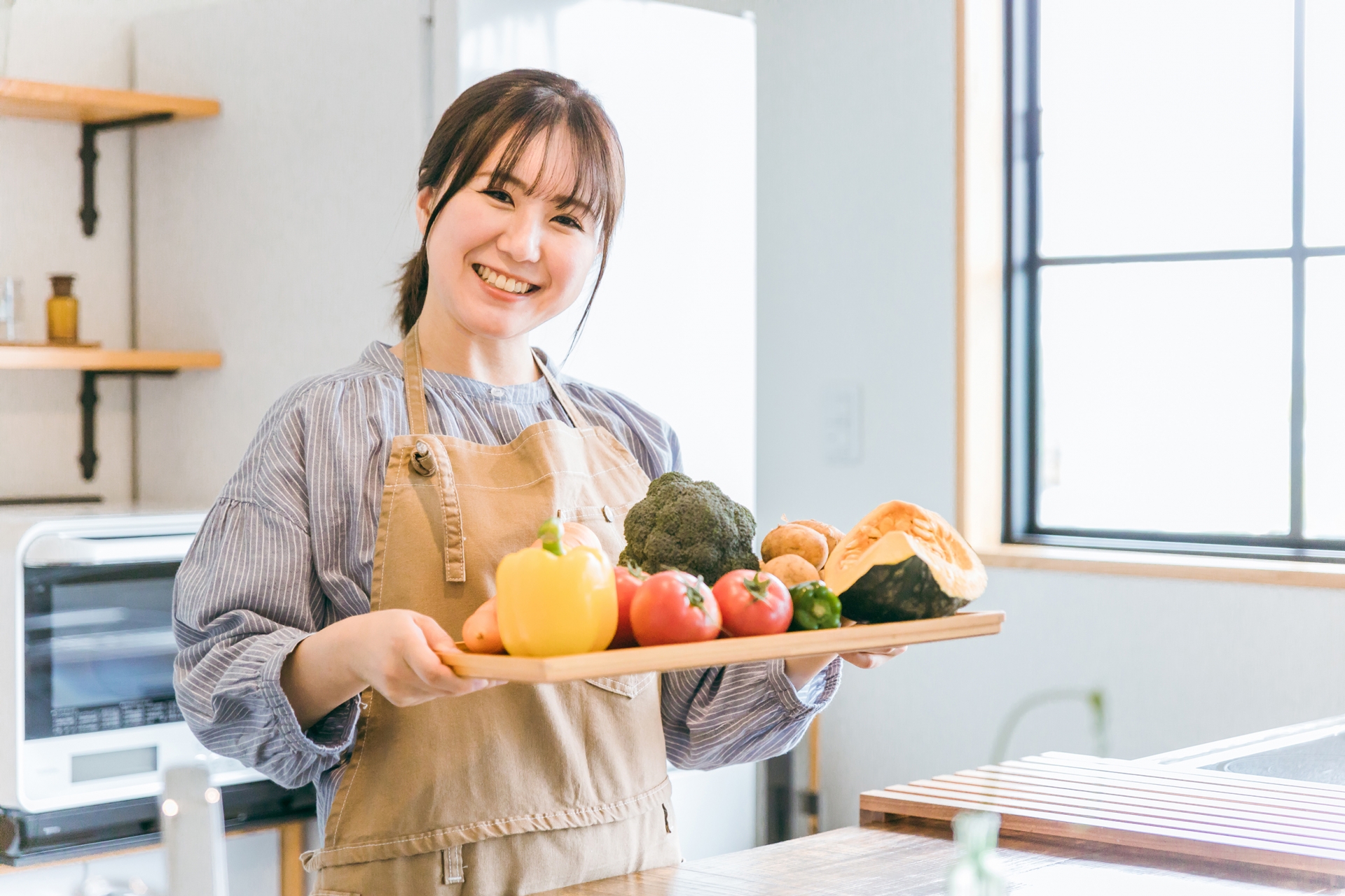 野菜を持ってキッチン立つエプロン姿の女性