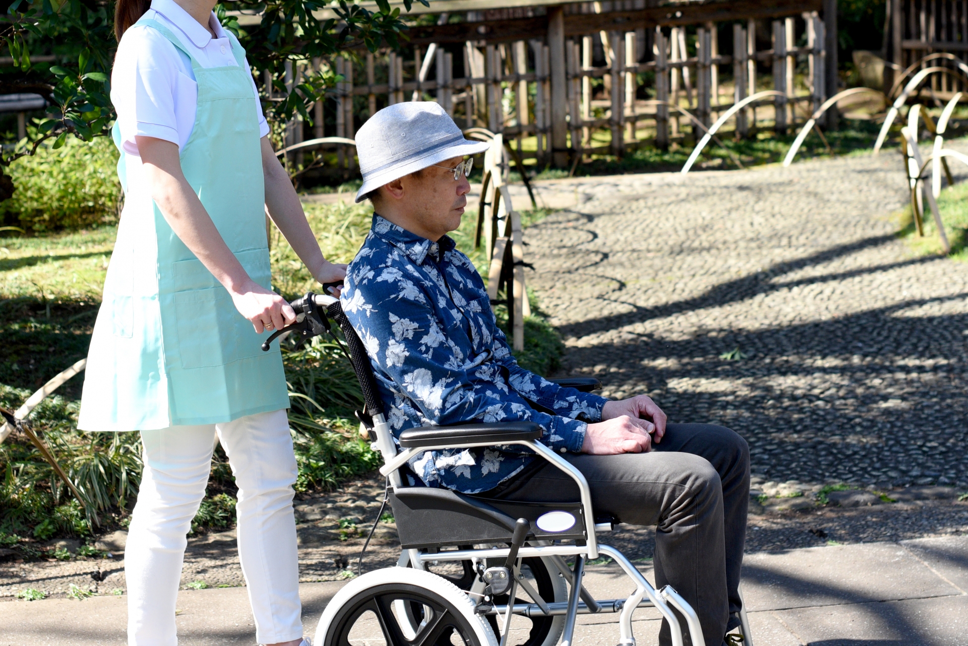 屋外で車椅子を押す若い介護士の女性とシニア男性
