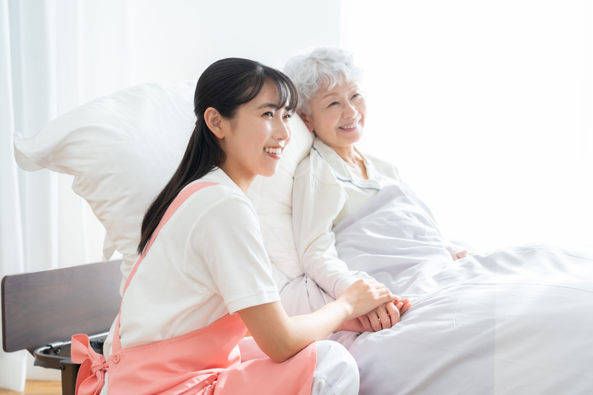 寝ているシニア女性を介護をする介護士