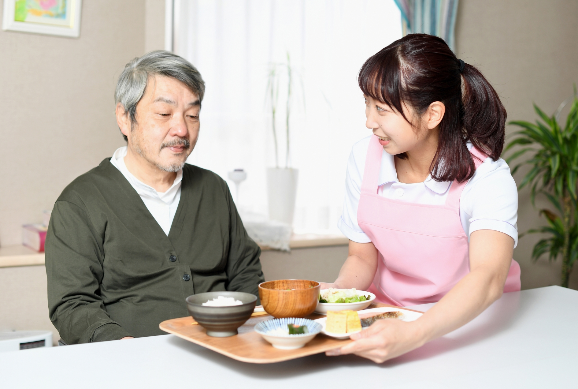 食事の配膳をする女性介護士と高齢者男性