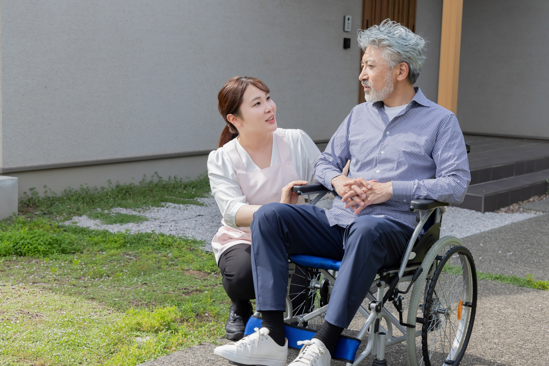 庭で車椅子に乗るシニア男性と介護士