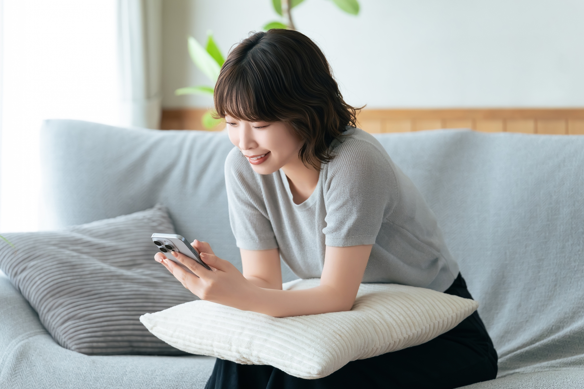 ソファに座ってスマホを使う笑顔の女性