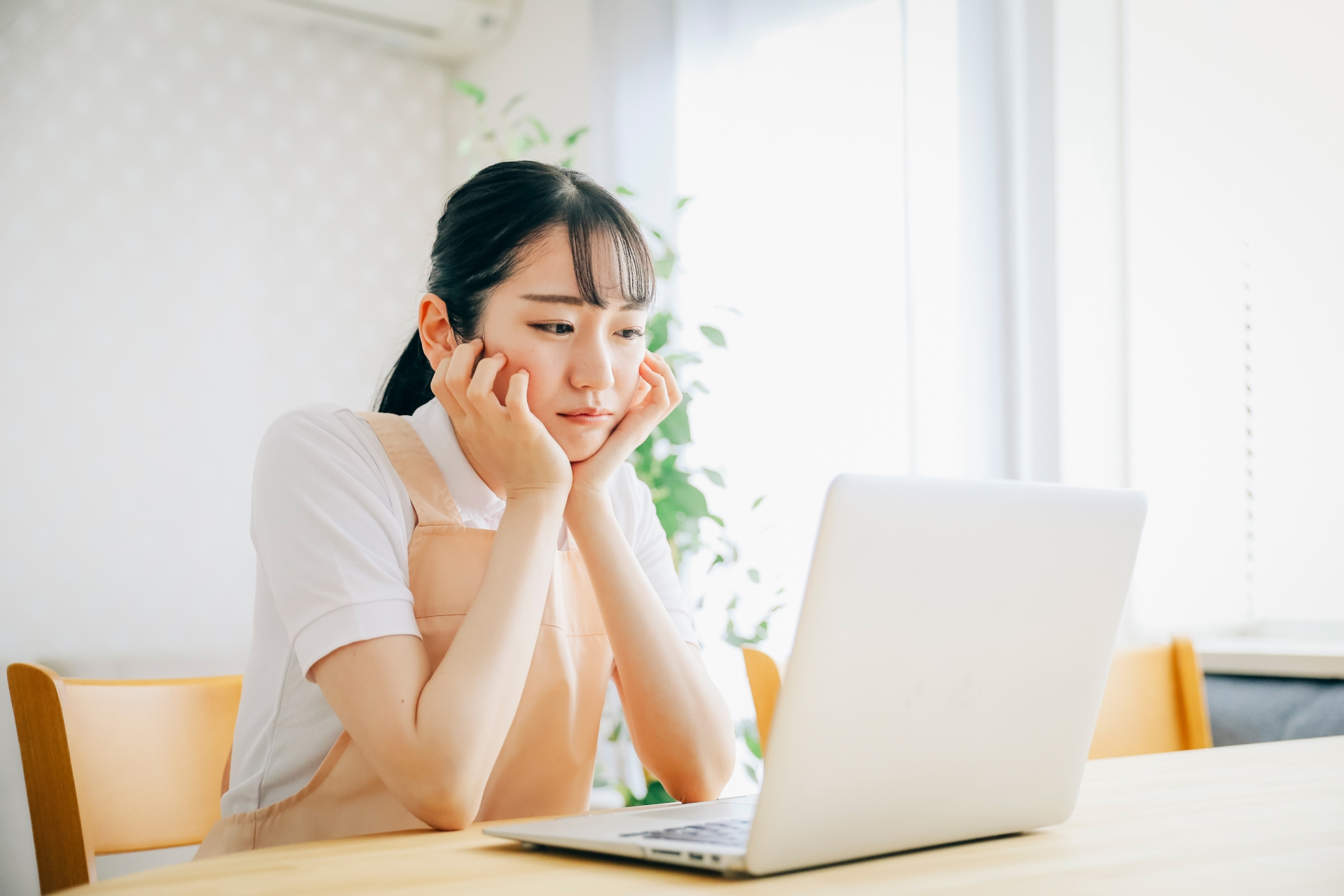 パソコンを使うエプロン姿の女性（考える・困る）
