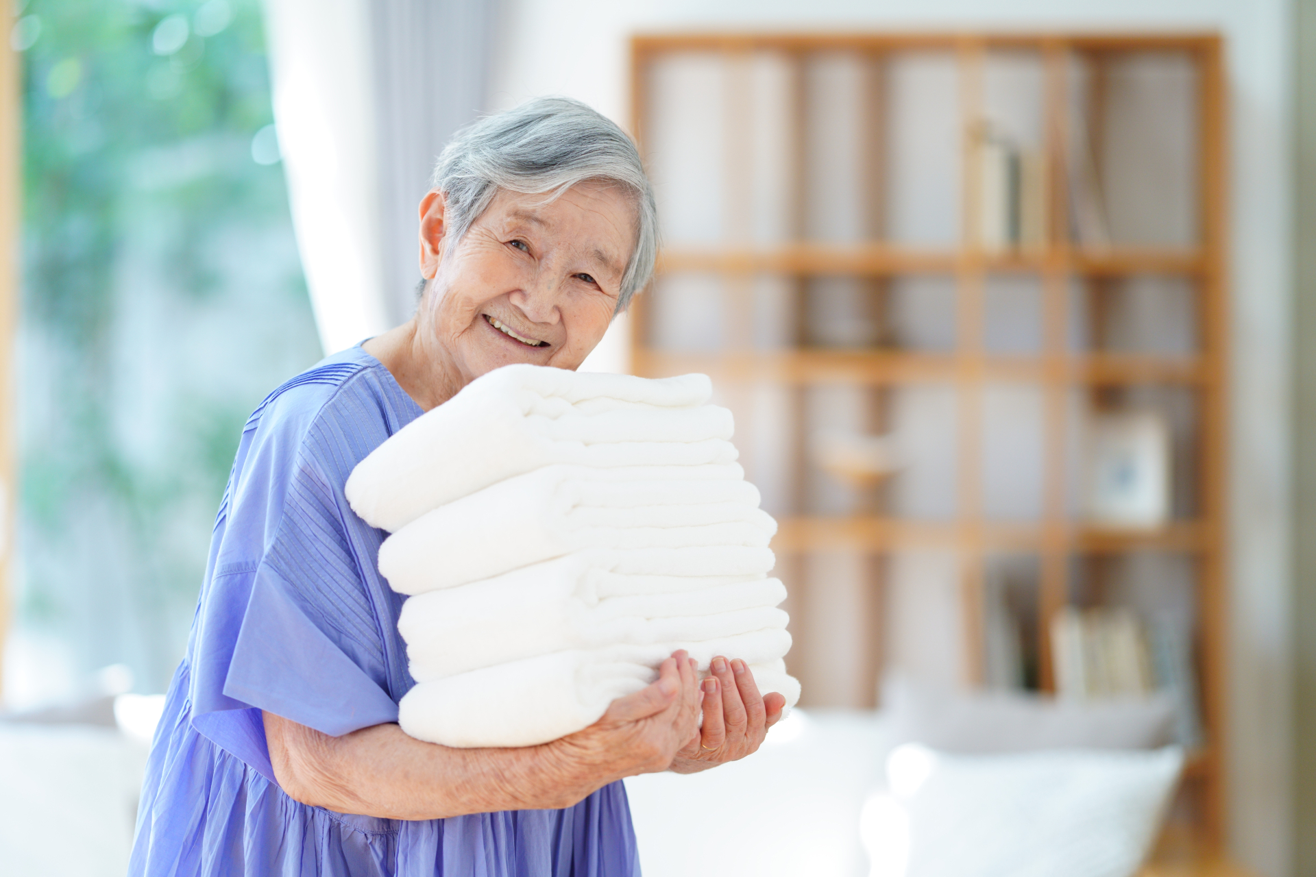 畳まれたタオルを運ぶ高齢女性