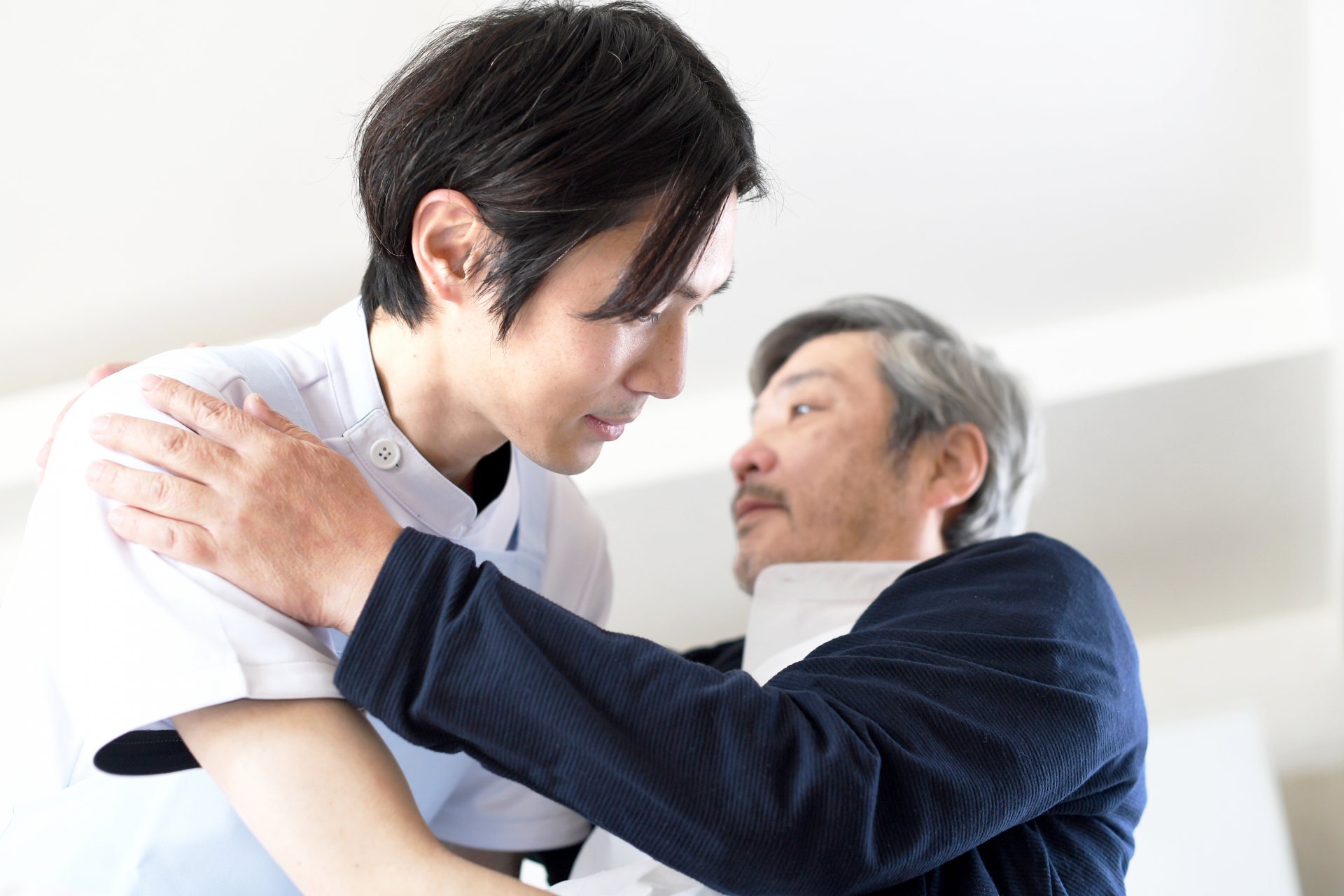 ベッドでお年寄りの男性を起こす介護士