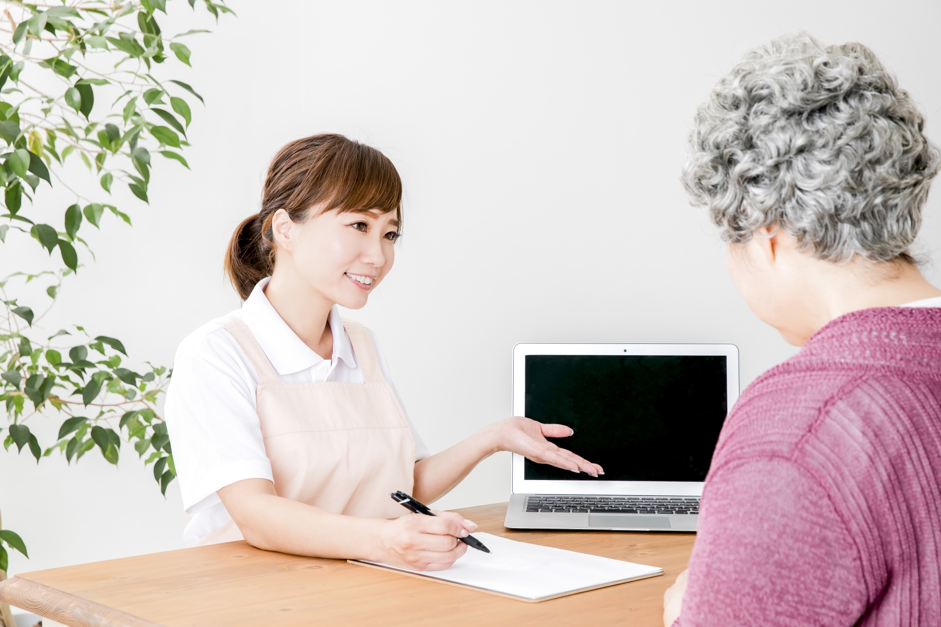ノートパソコンで説明する介護士と高齢者の女性