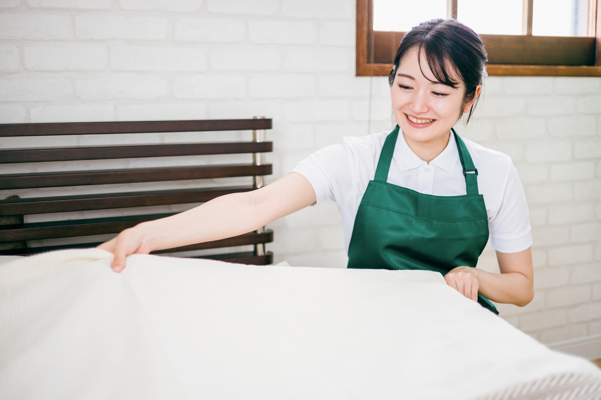 ベッドメイキングする客室清掃員の女性