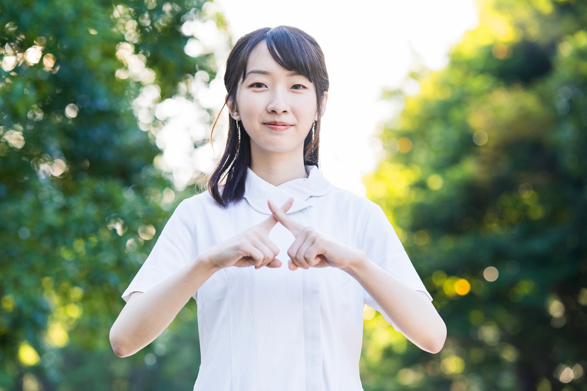 「バツ」のポーズをする白衣の女性
