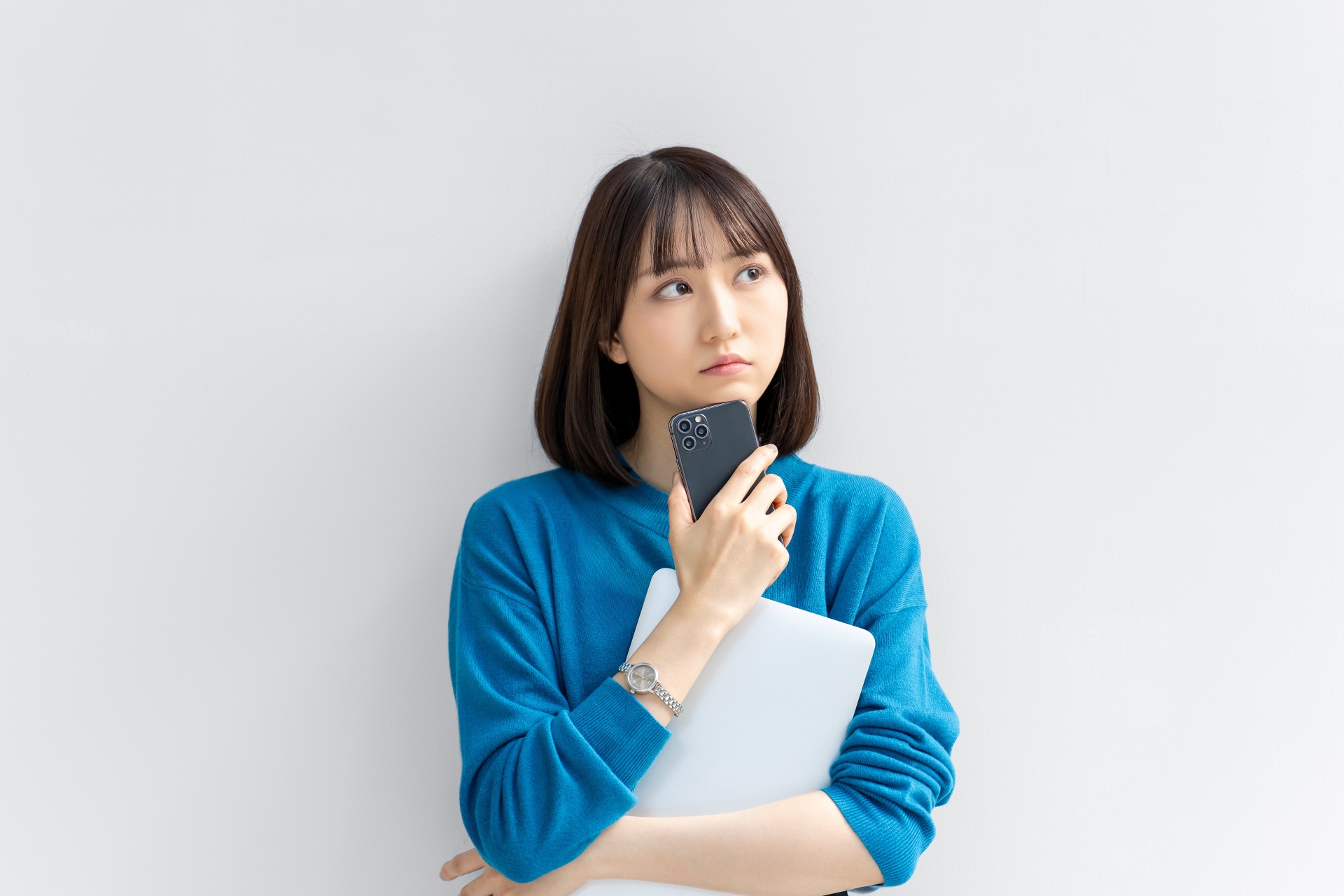スマホとパソコンを持って考える女性