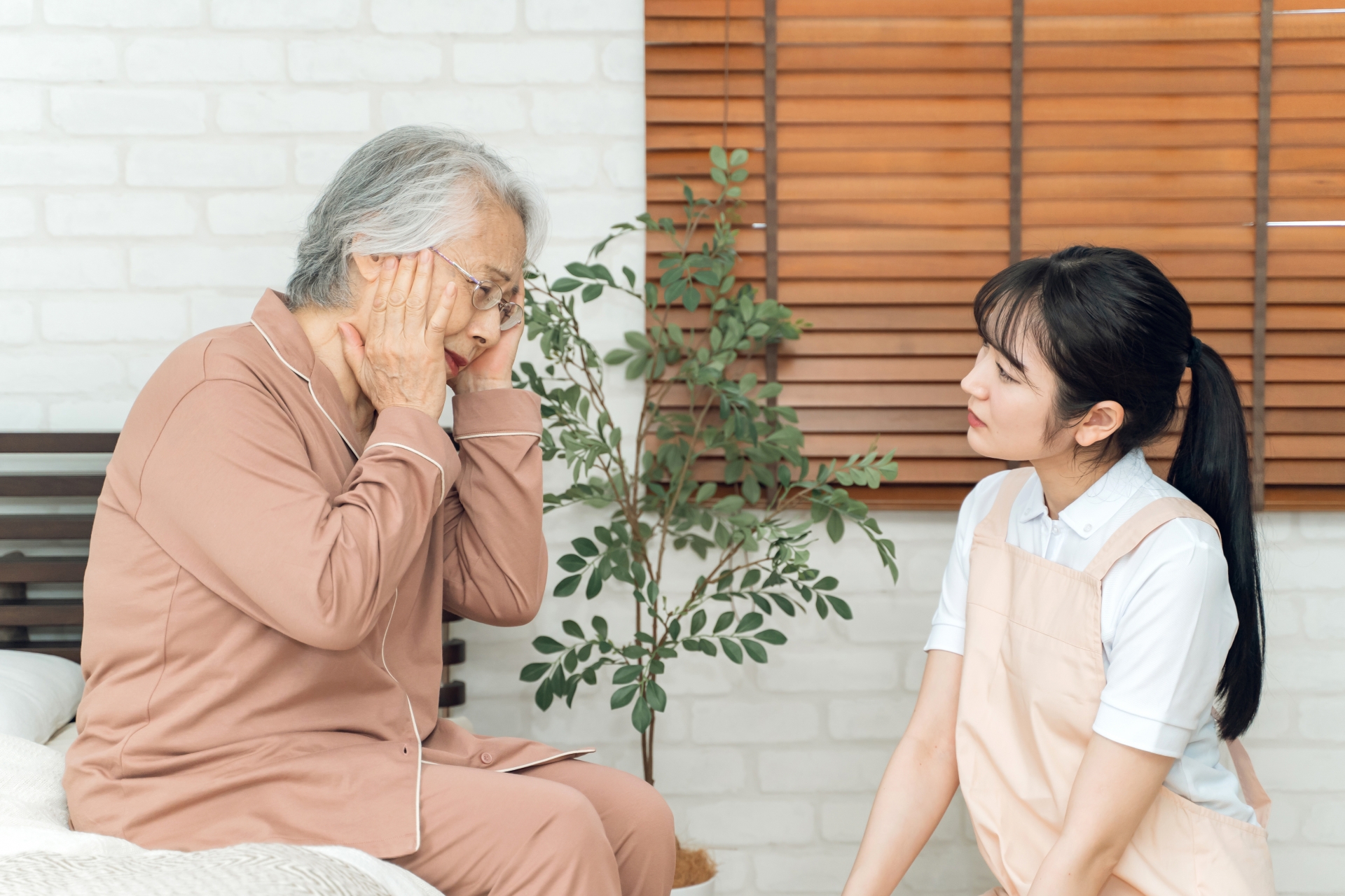 痛がる高齢者女性とエプロン姿の女性(頭痛)