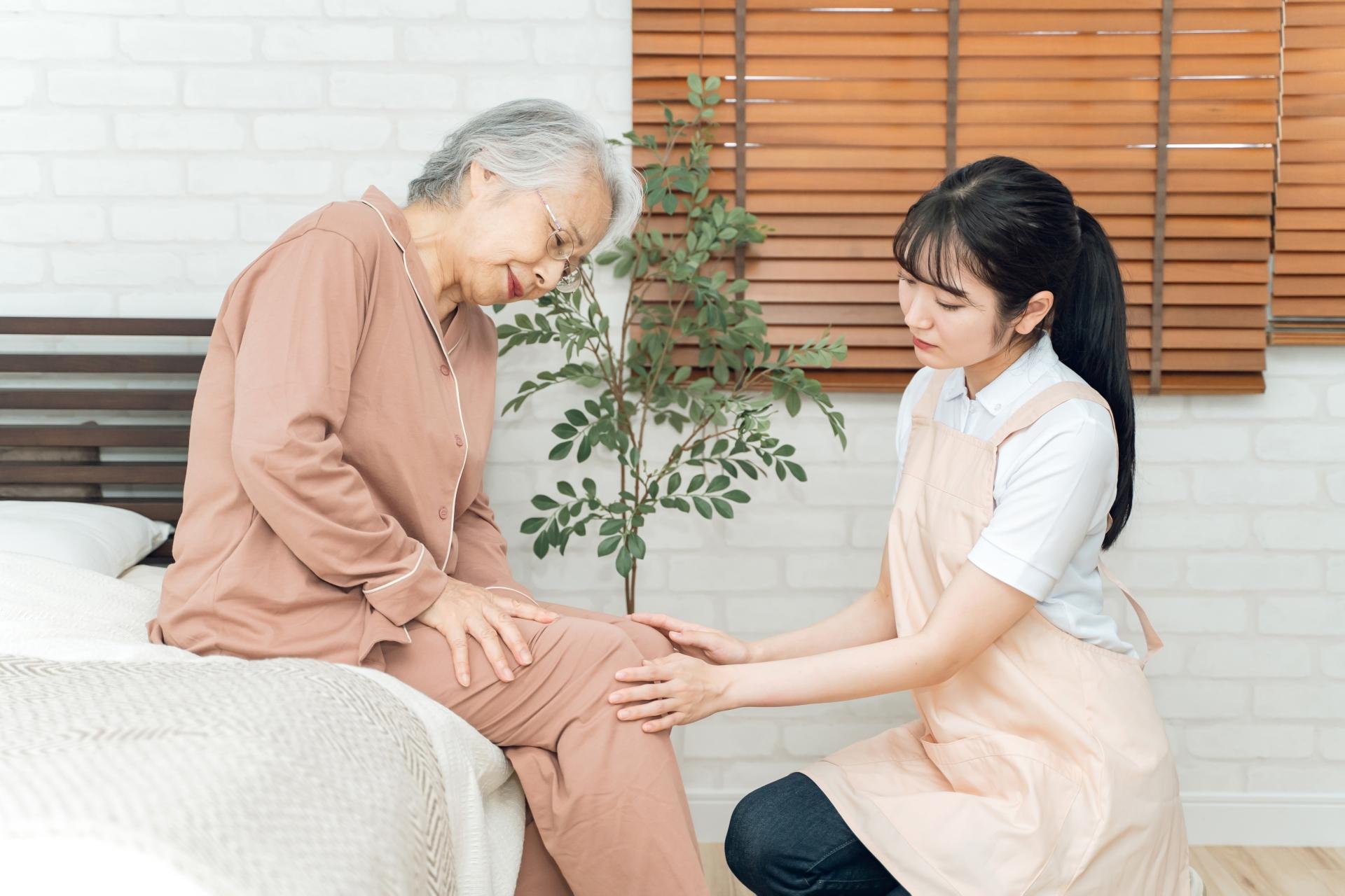痛がる高齢者女性と介護士(膝痛)