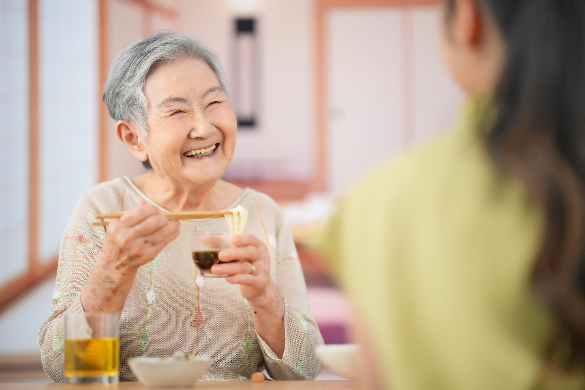 向かい合ってそうめんを食べるおばあちゃんと女性の後ろ姿